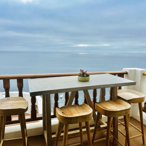 - Enjoy serene ocean panoramas from this stylish balcony dining nook
- Elegant concrete top table paired with natural wood stools invites alfresco meals
- Succulent centerpiece adds a charming, coastal touch to the peaceful setting